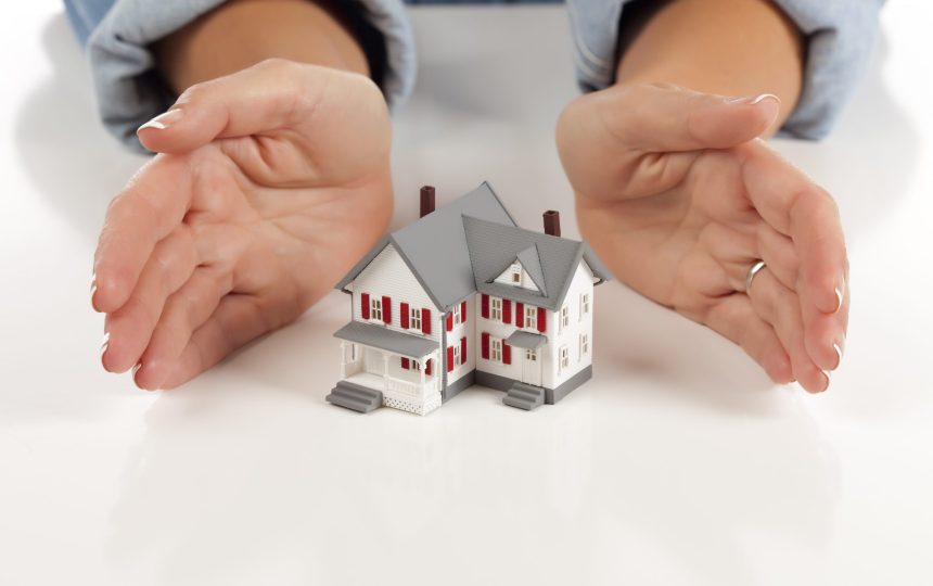 Womans Hands Around Model House on White Surface.